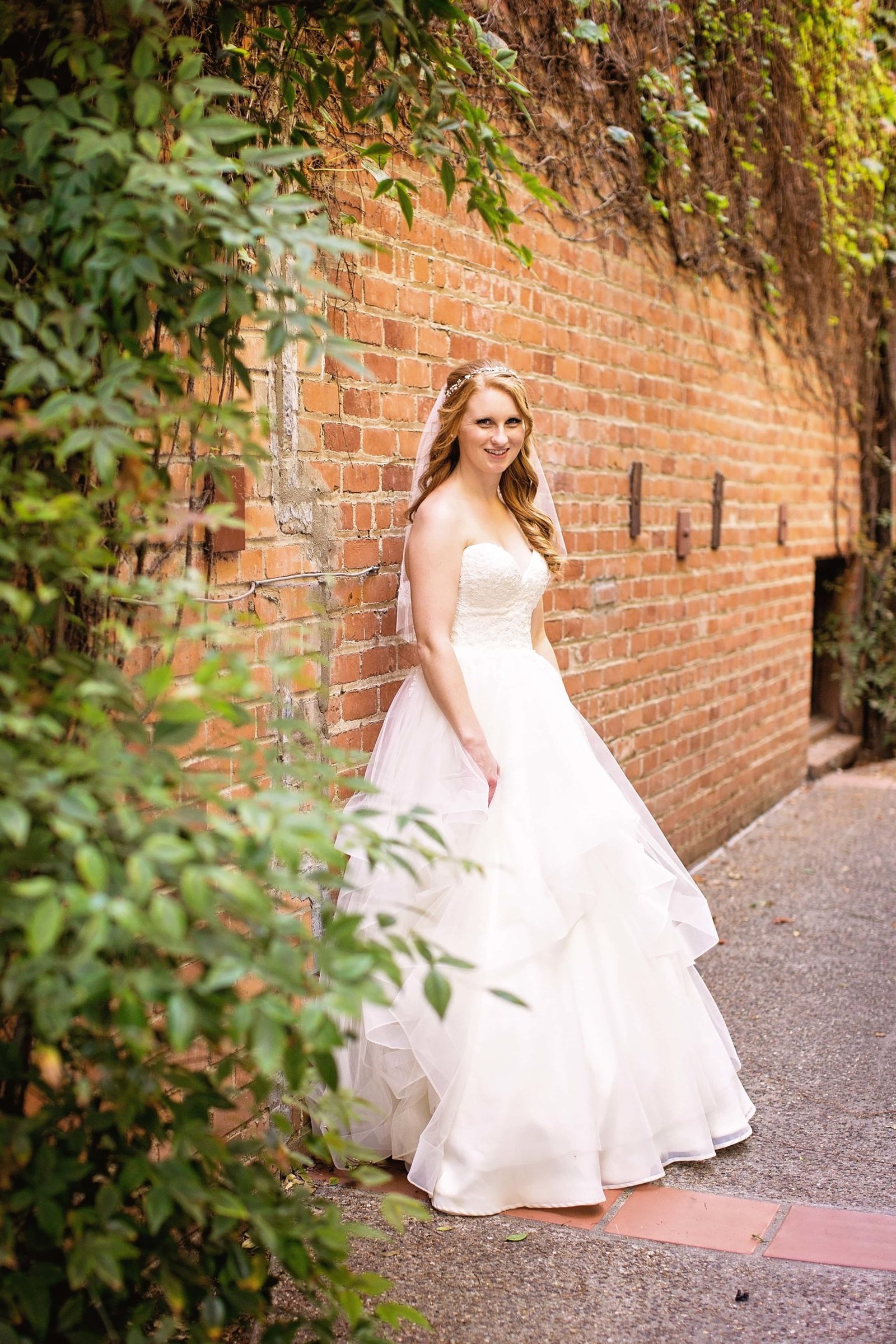 Bride looking at the camera while leaning on a red brick wall at Heritage House in Arroyo Grande