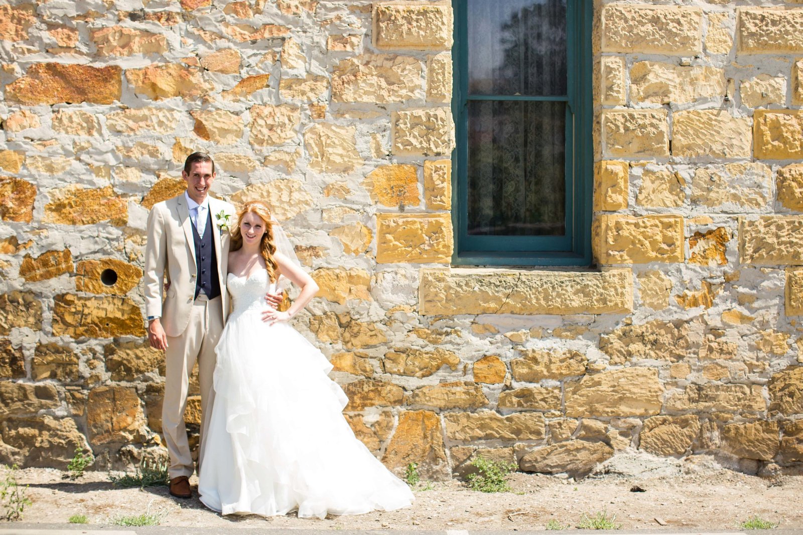 Bride and groom pose for a portrait in front of a stone wall at Heritage House in Arroyo Grande
