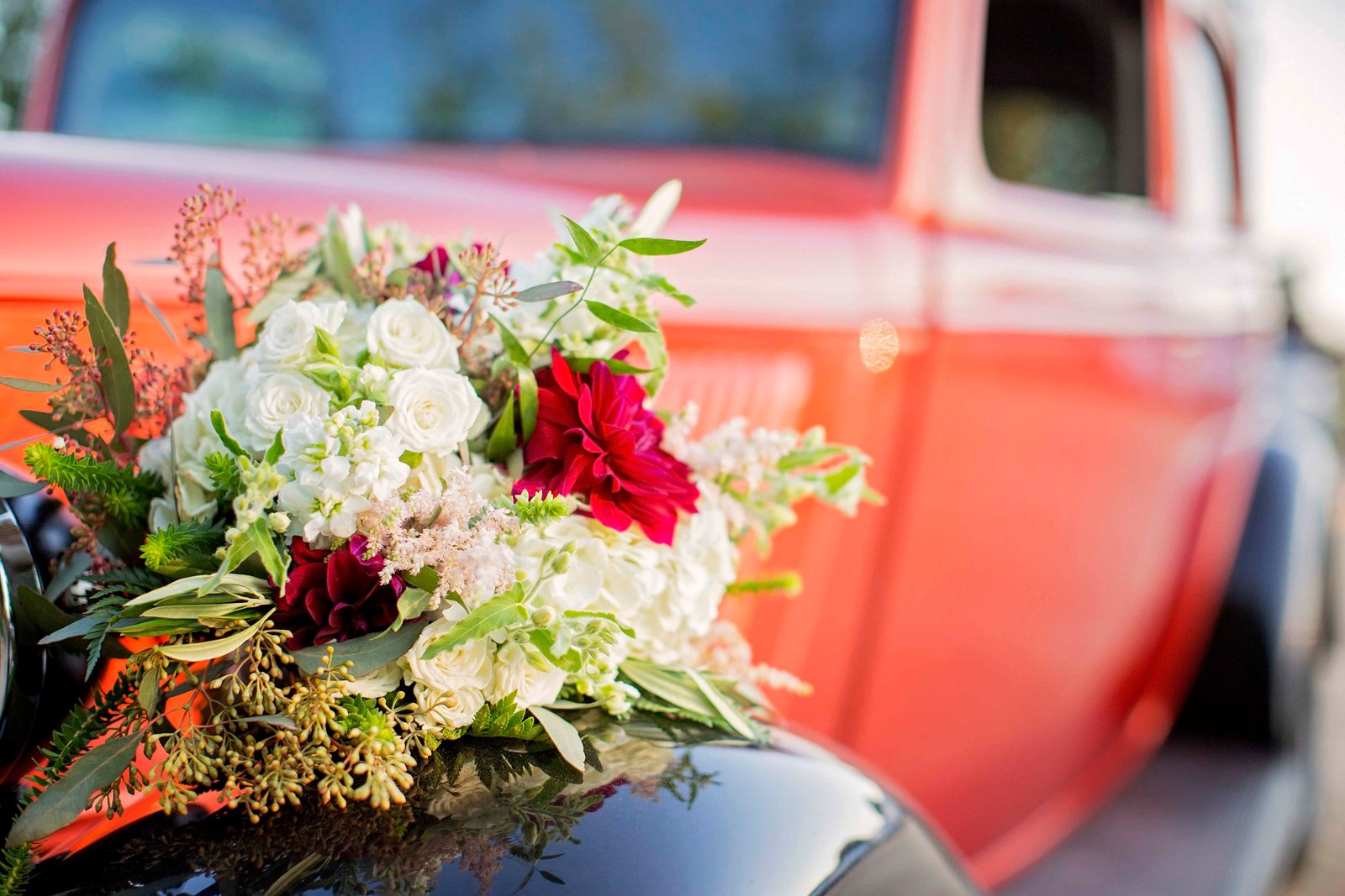 Bridal bouquet on the fender of an orange classic car