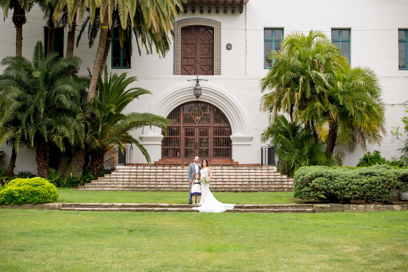 Pulled back photo of bride and groom standing with flower girl at the Santa Barbara Courthouse