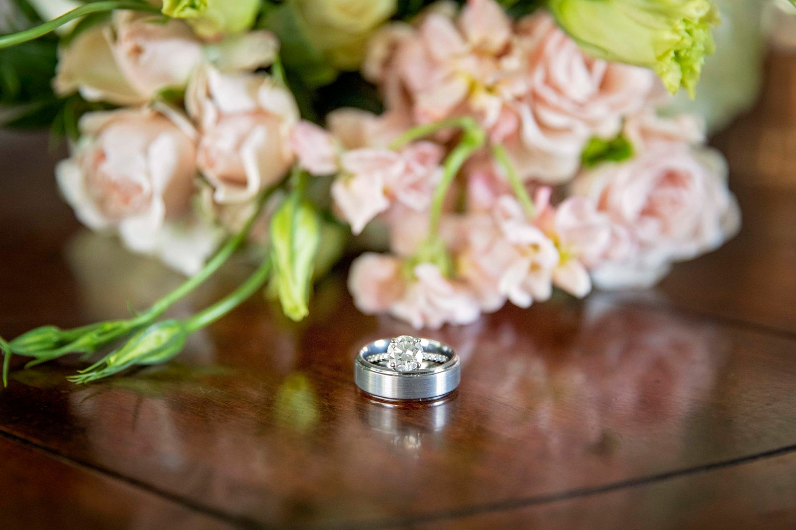 wedding rings on a wood table in front of the bouquet