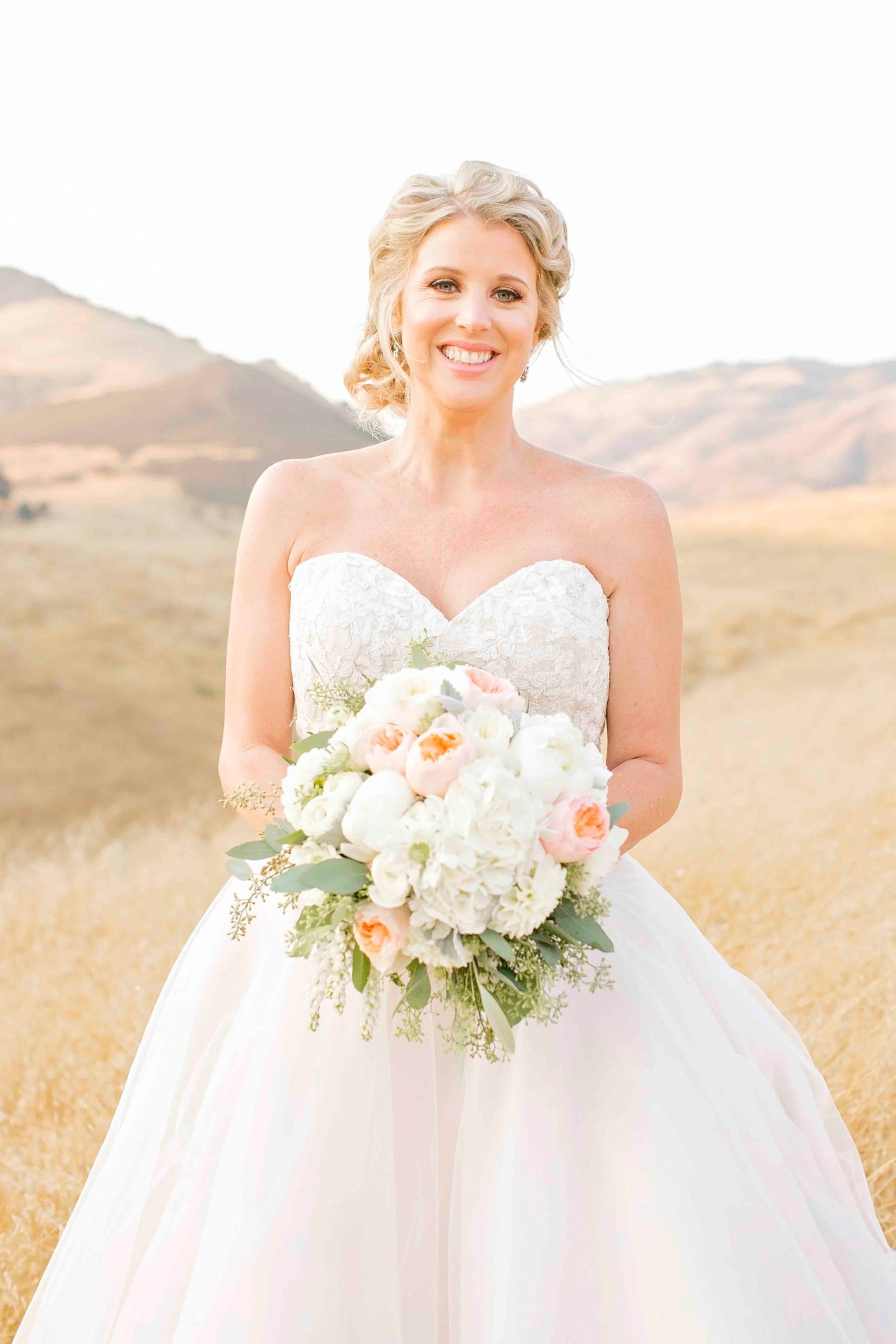 Bride holding her bouquet in an open field at Higuera Ranch