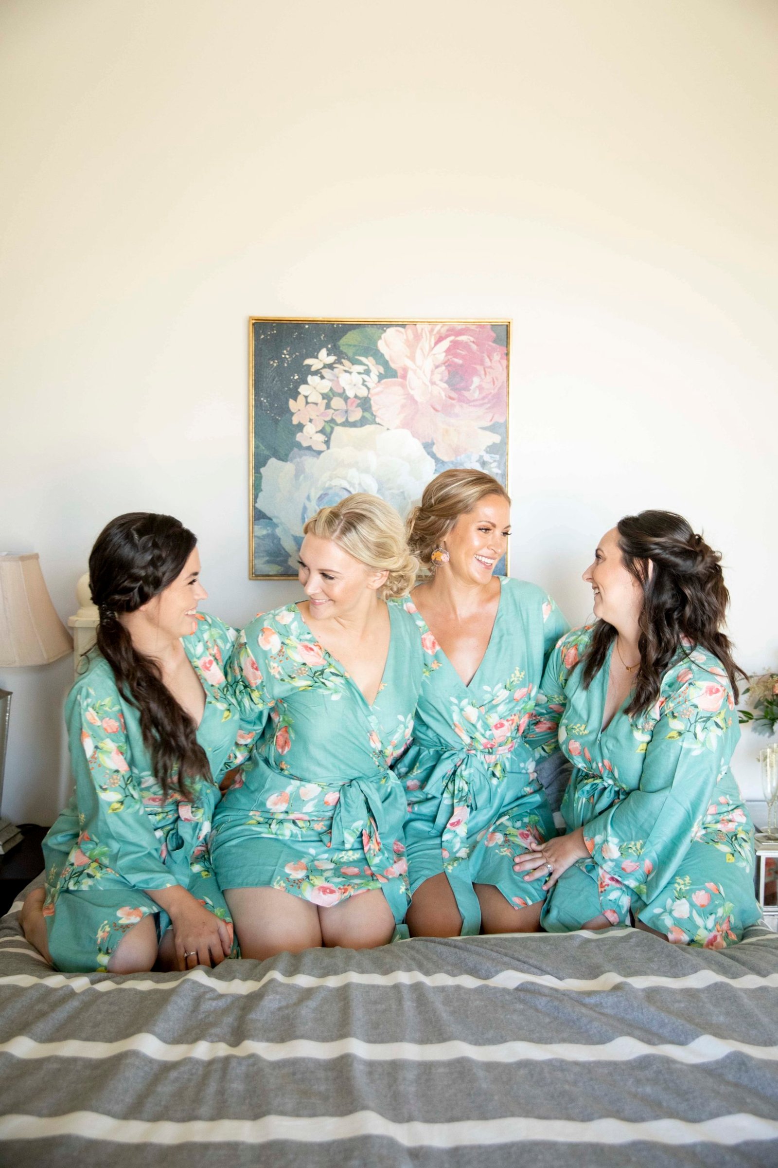 Bride and bridesmaids smiling while wearing matching robes on a bed