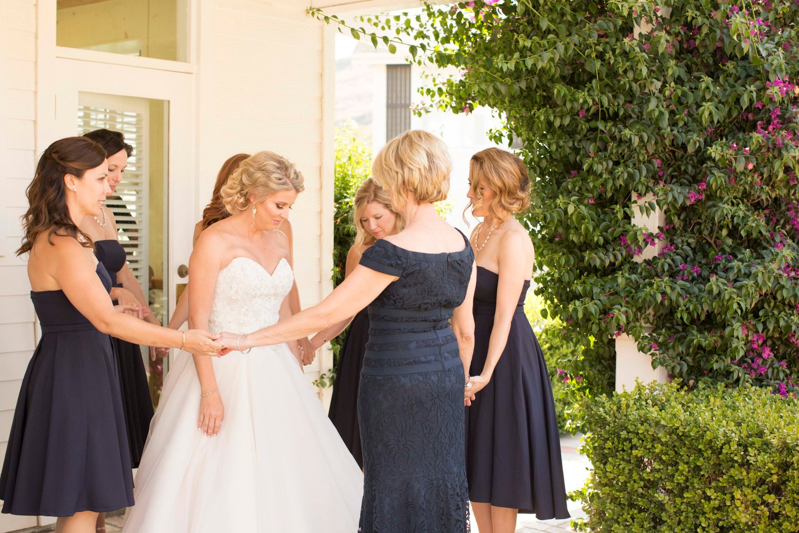 Bridesmaids holding hands in a circle around the bride while praying for her at Higuera Ranch