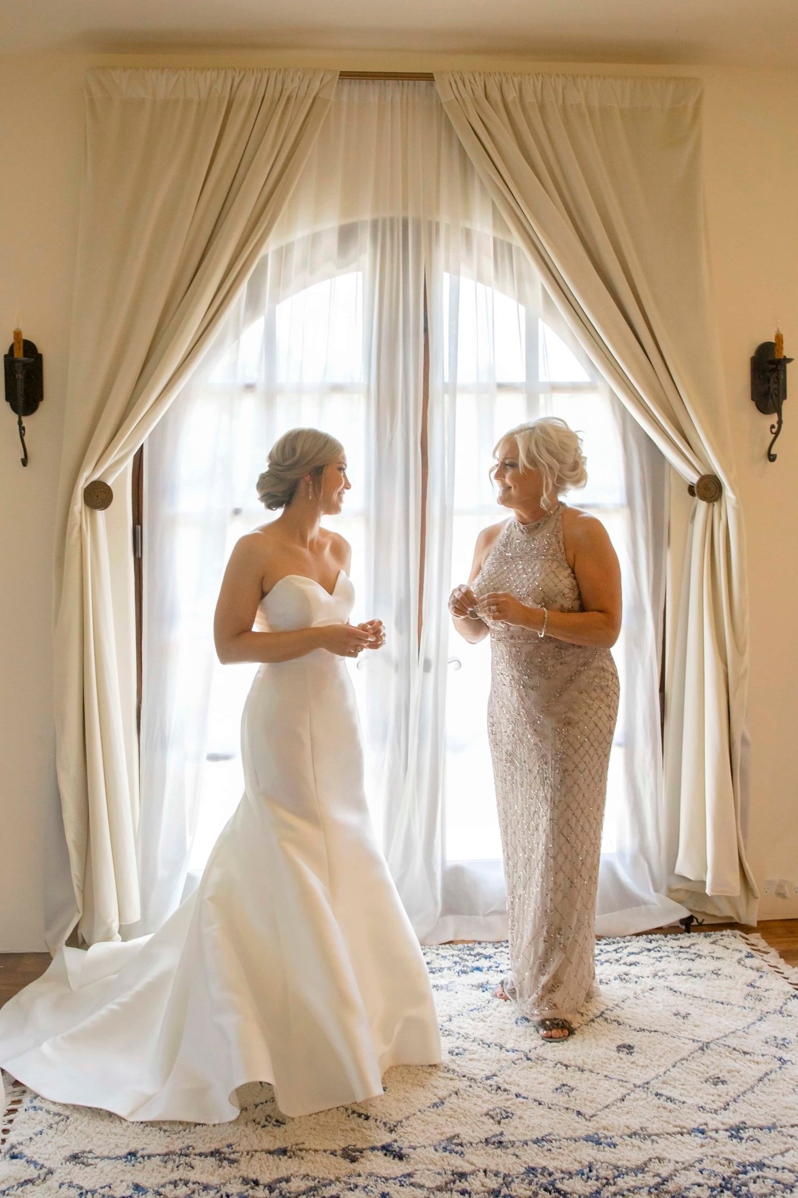 Bride talking with her mother in front of backlit French doors