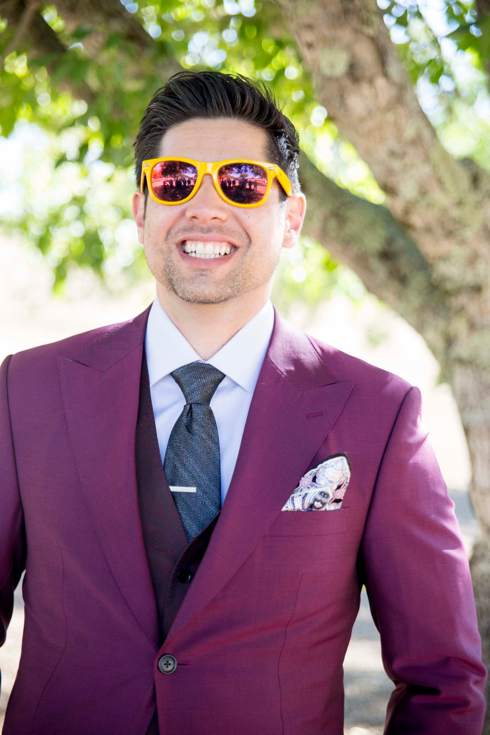 groom smiling at the camera wearing a burgundy suit and yellow sunglasses