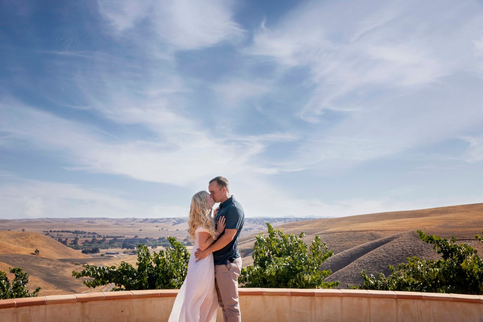 couple kissing with the California hillside and blue skies in the background