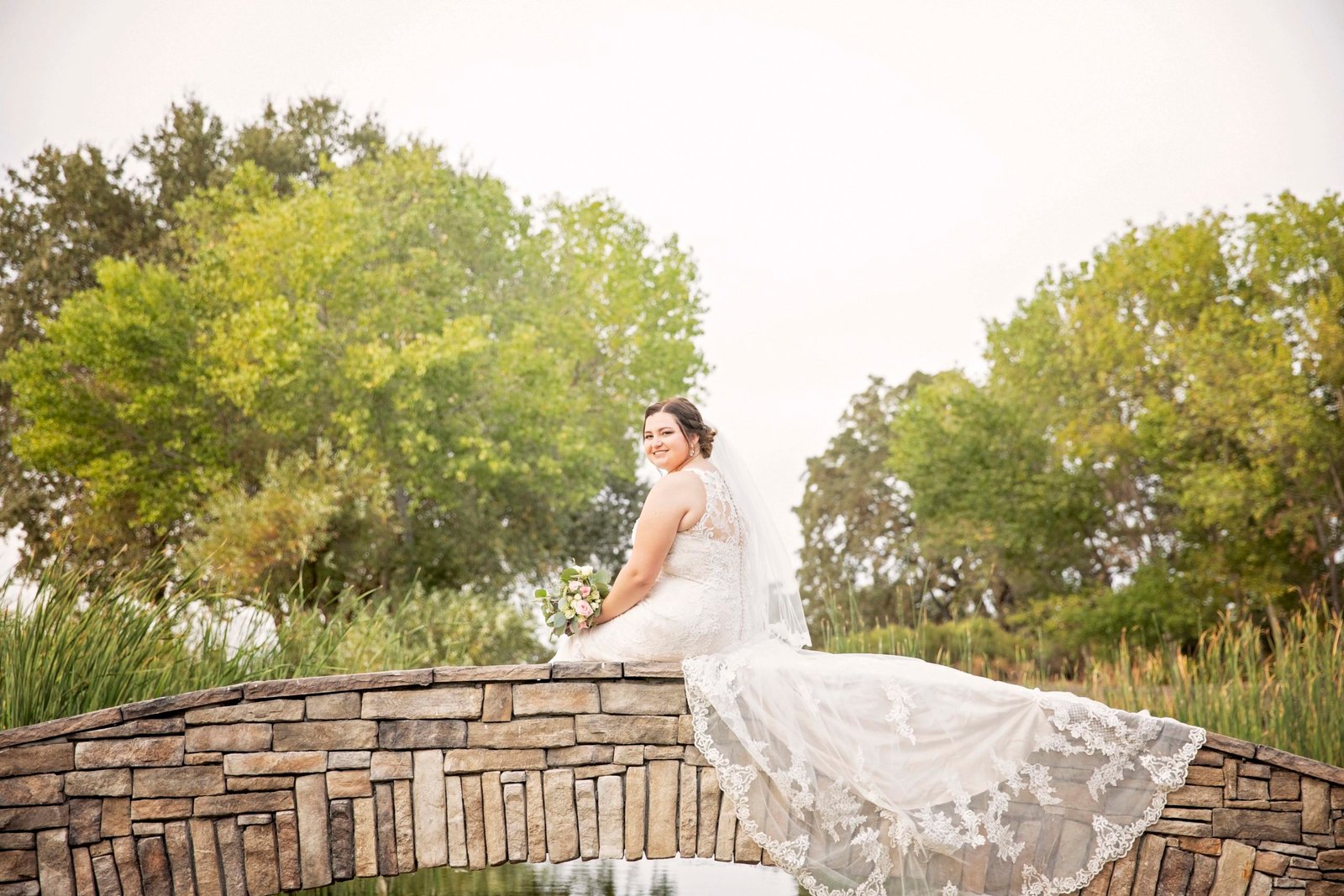 Bride sitting on stone bridge with dress overhanging at Fallen Oaks Estate