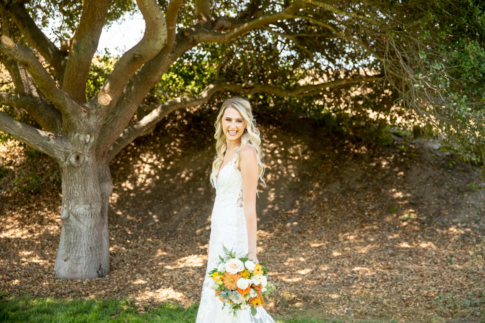bride in front of an oak tree holding her bouquet looking at the camera