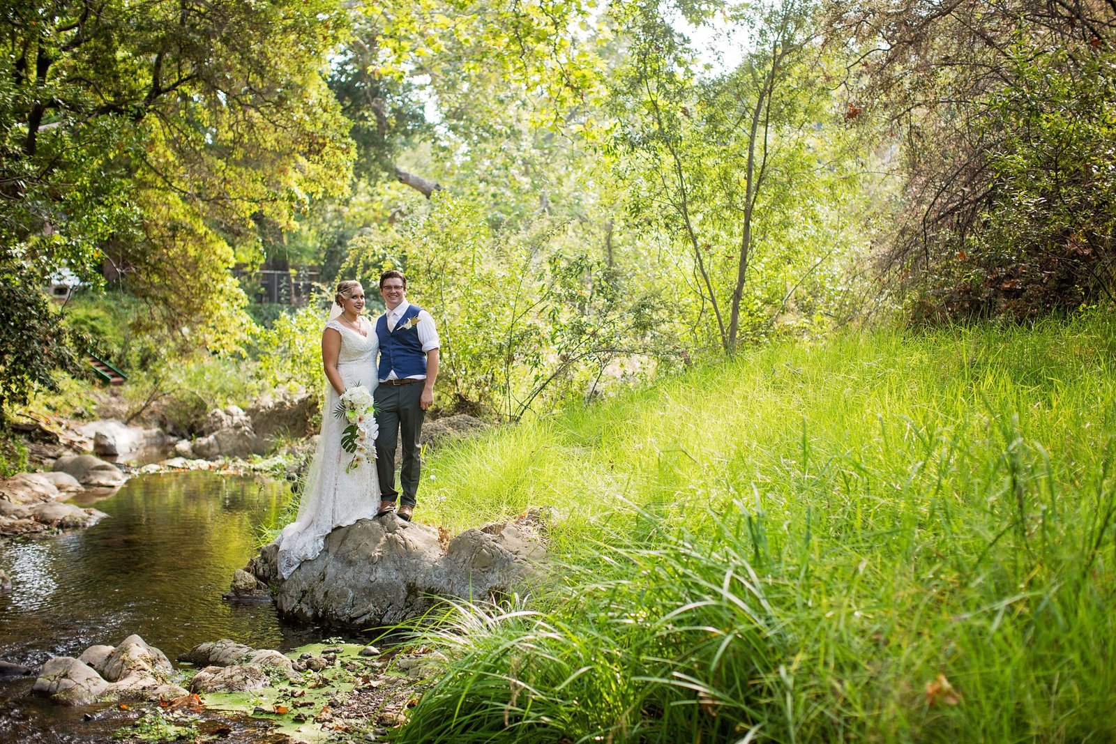 Bride and groom standing on a boulder in the creek at The Monday Club
