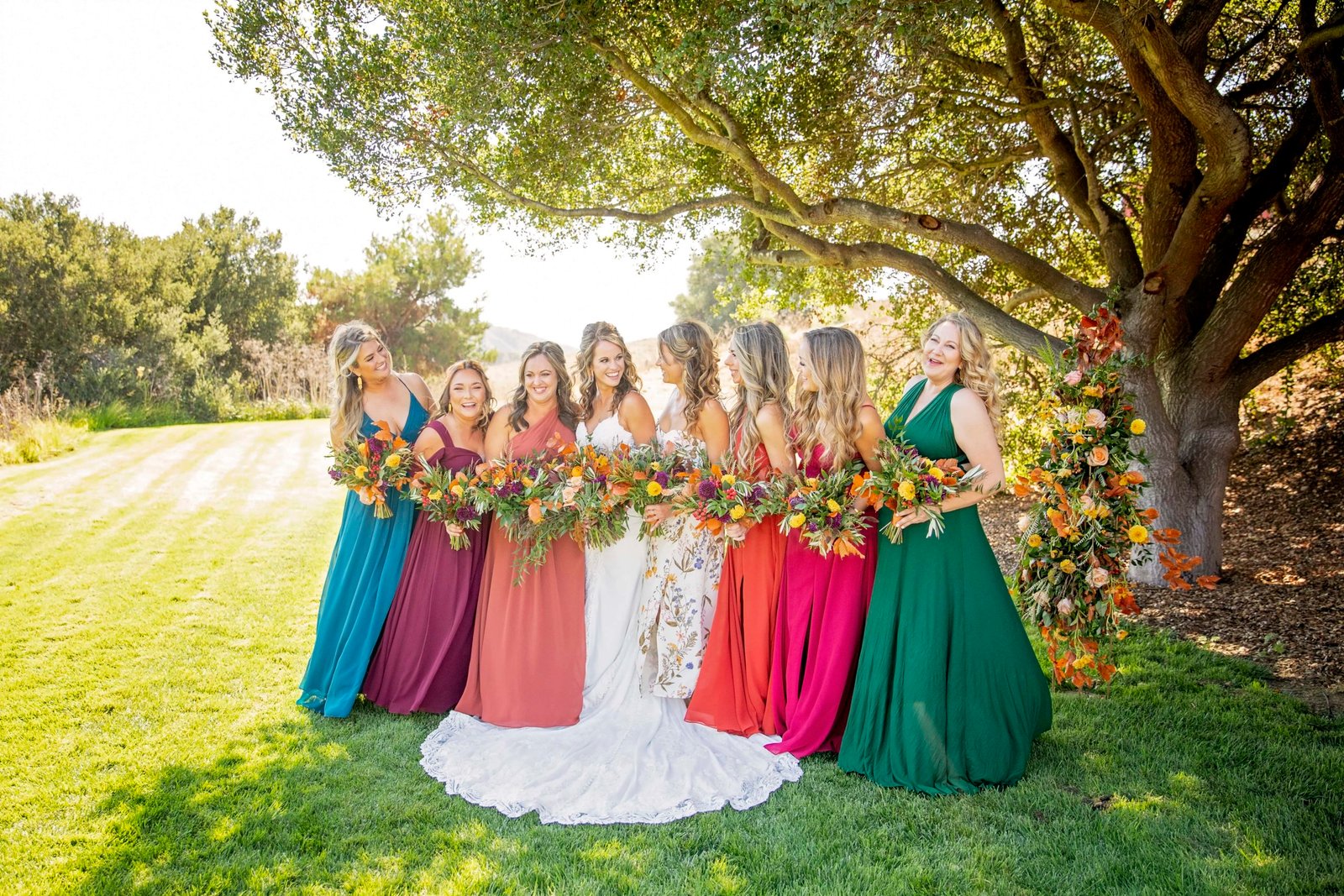 Bride laughs with her bridesmaids dressed in vibrant fall colors at Loma Grande Ranch