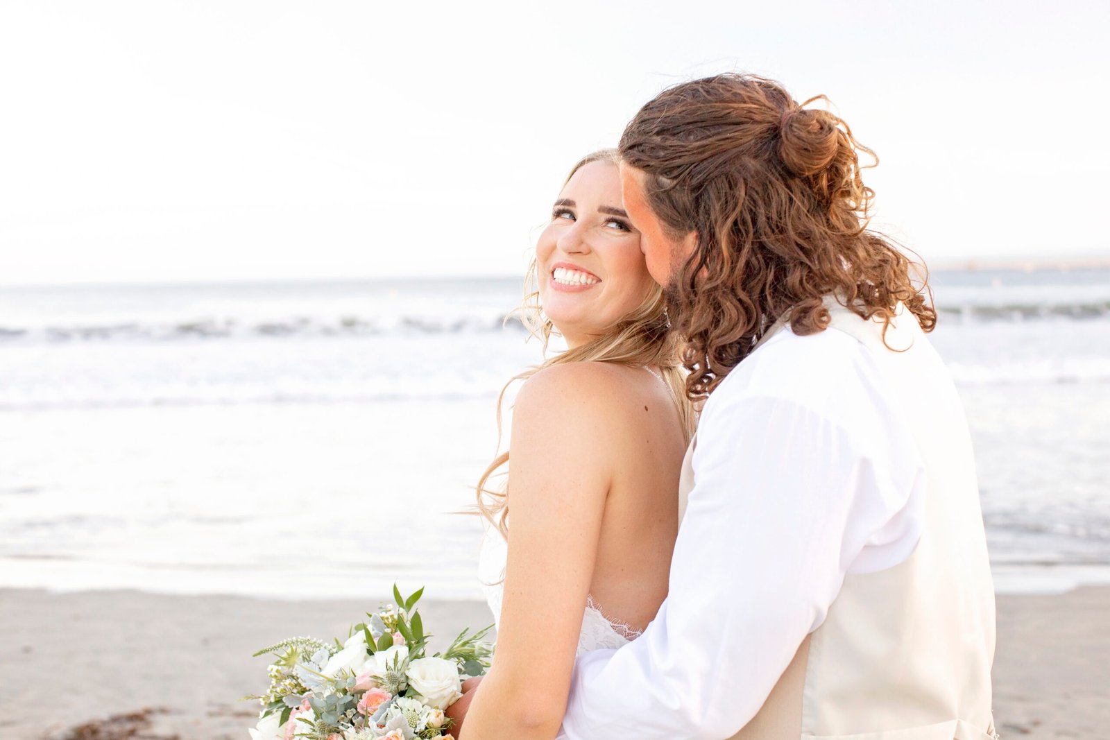 bride smiling on the beach while looking up at the groom