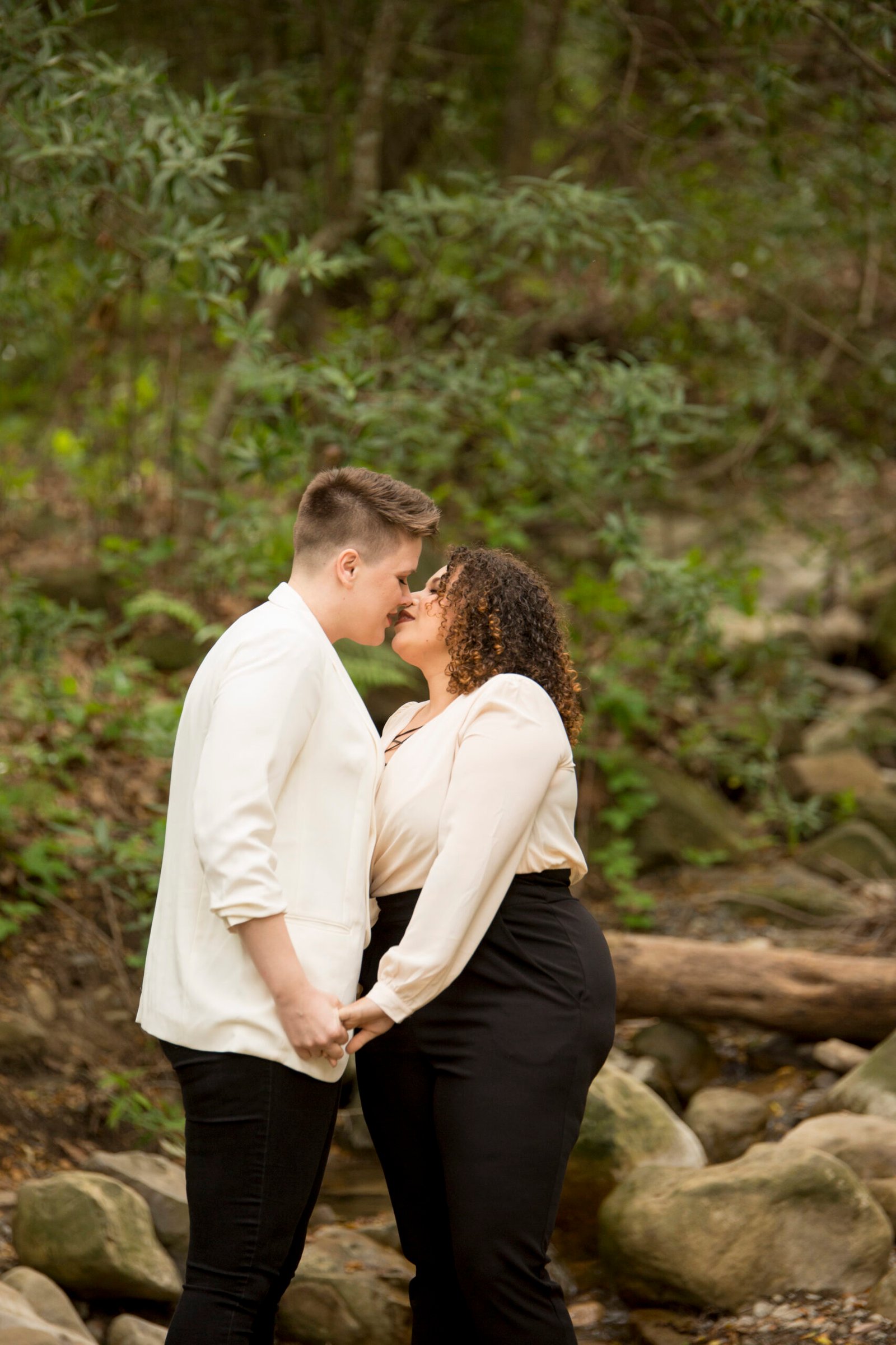 Two women kissing during an engagement session on a trail