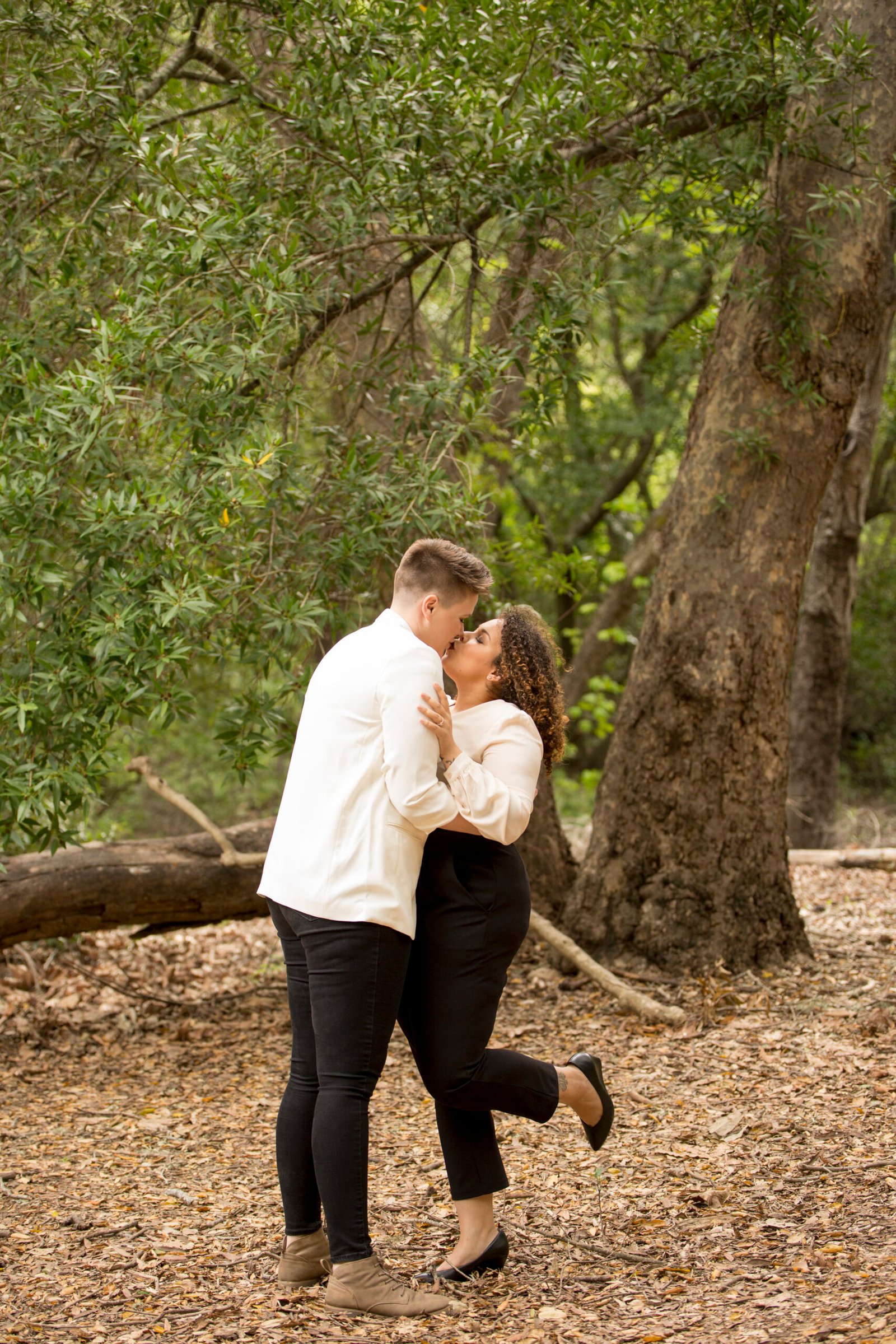 two brides kiss on a trail in front of large oak trees