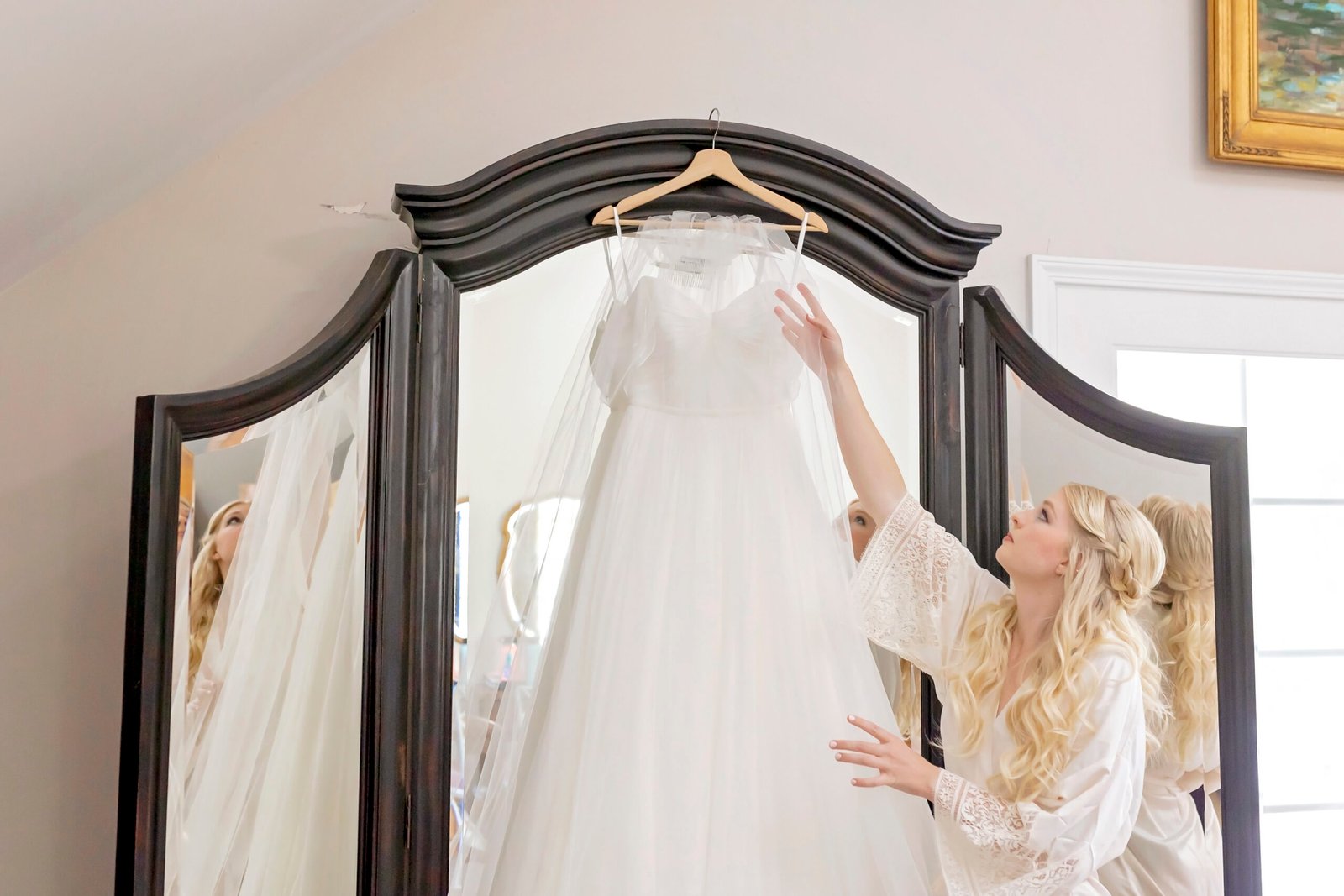 bride admiring her wedding dress hanging on a mirror