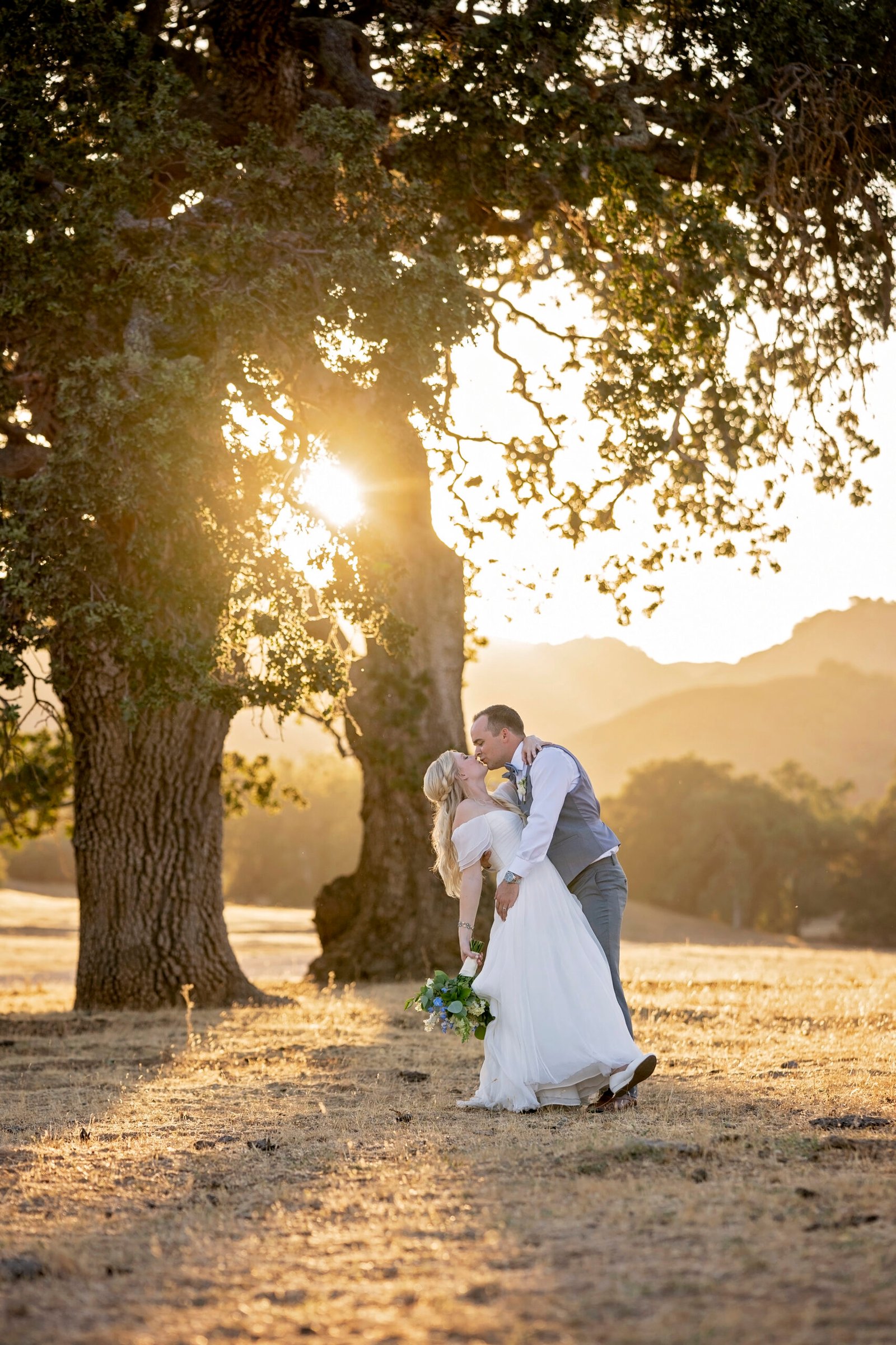 bride and groom kissing in a field with oak trees