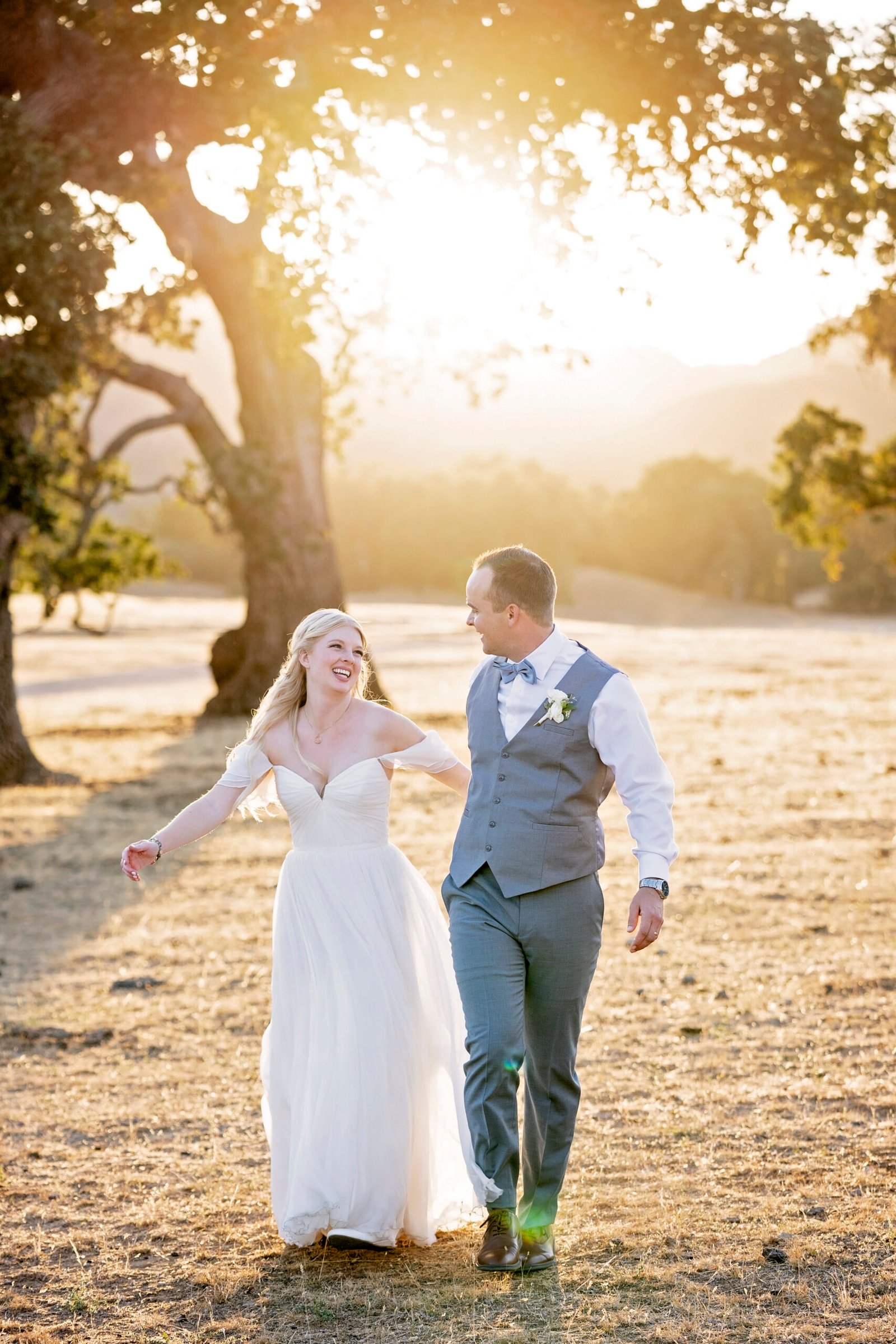bride and groom laughing in an open field with oak trees
