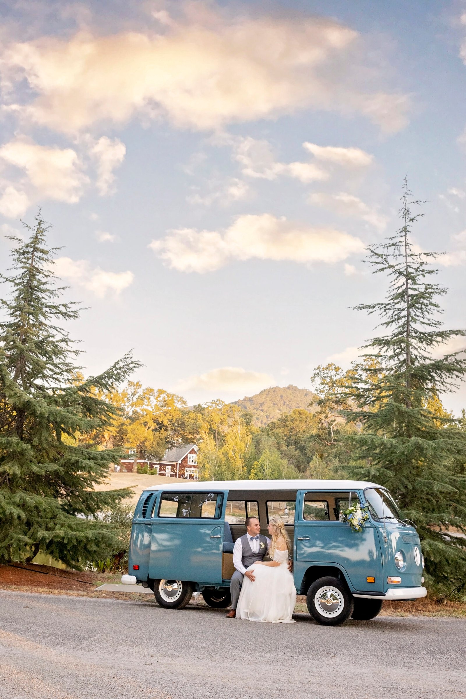 Bride and groom sit together in a VW Bus in front of Spanish Oaks Ranch