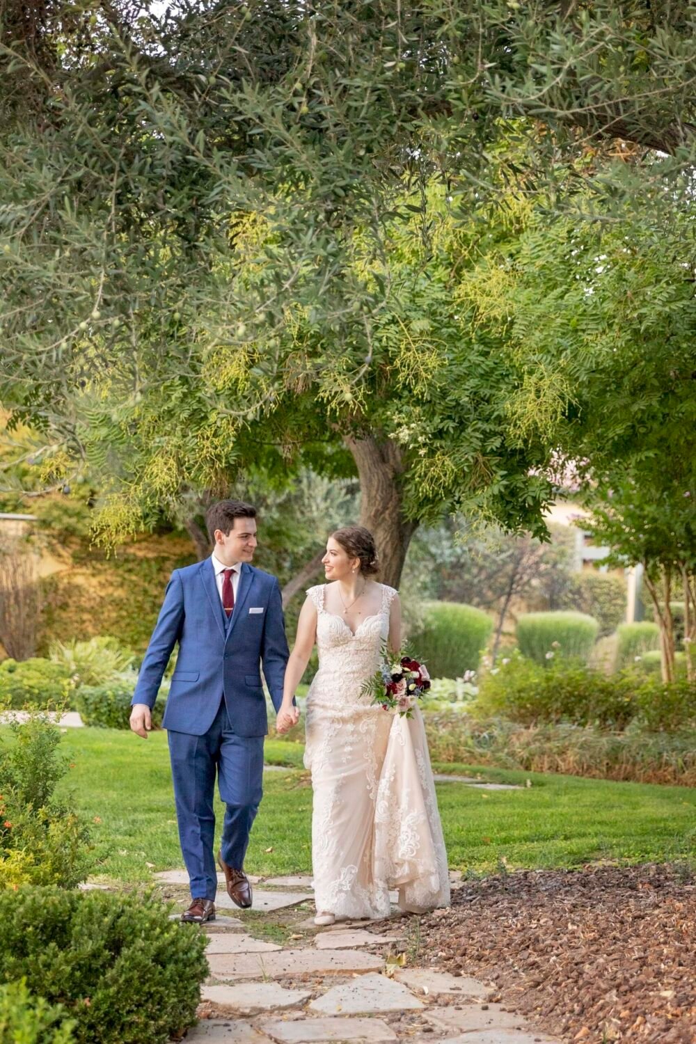 bride and groom holding hands while looking at each other and walking down a stone path