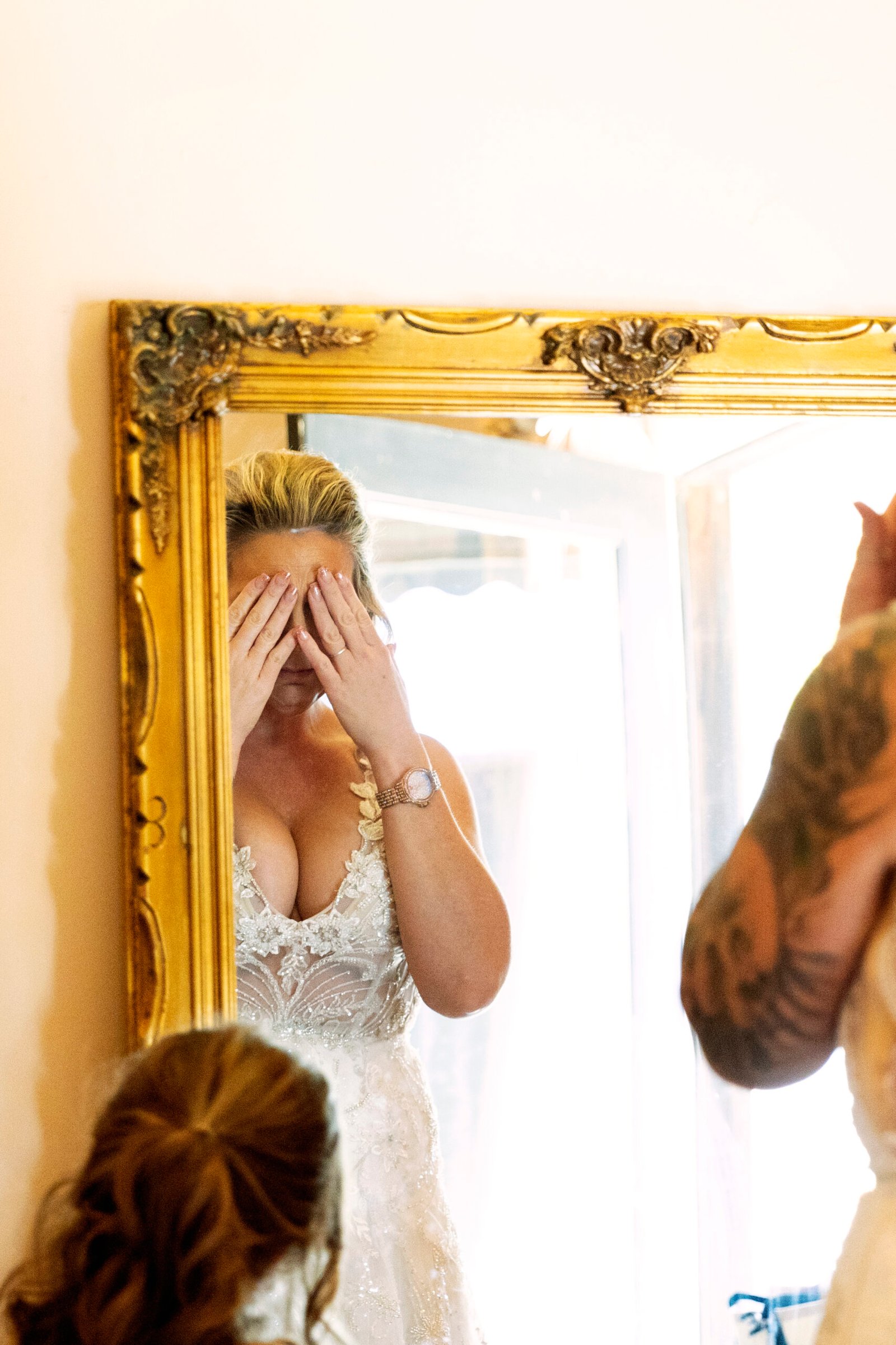 bride covering her eyes while looking in the mirror