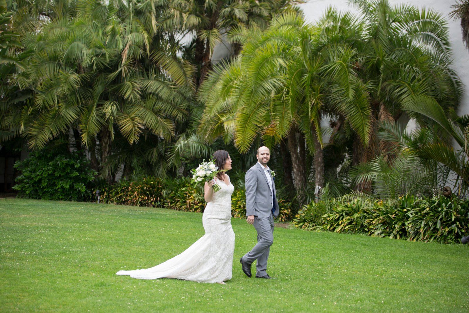 Bride and groom walking along the grass with palm trees behind them at the Santa Barbara Courthouse