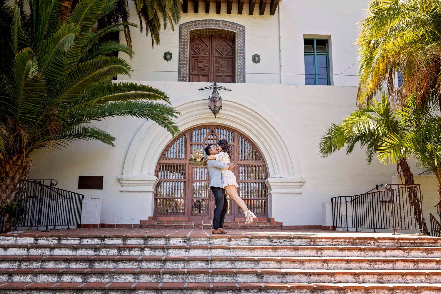 groom lifting the bride in front of an arched doorway at the Santa Barbara Courthouse