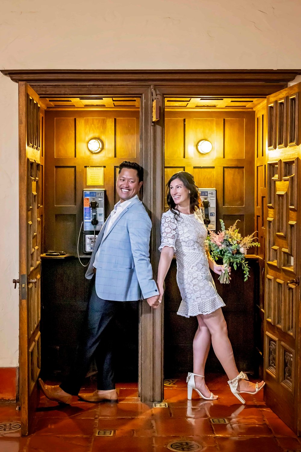 bride and groom standing in side by side phone booths while looking back at each other
