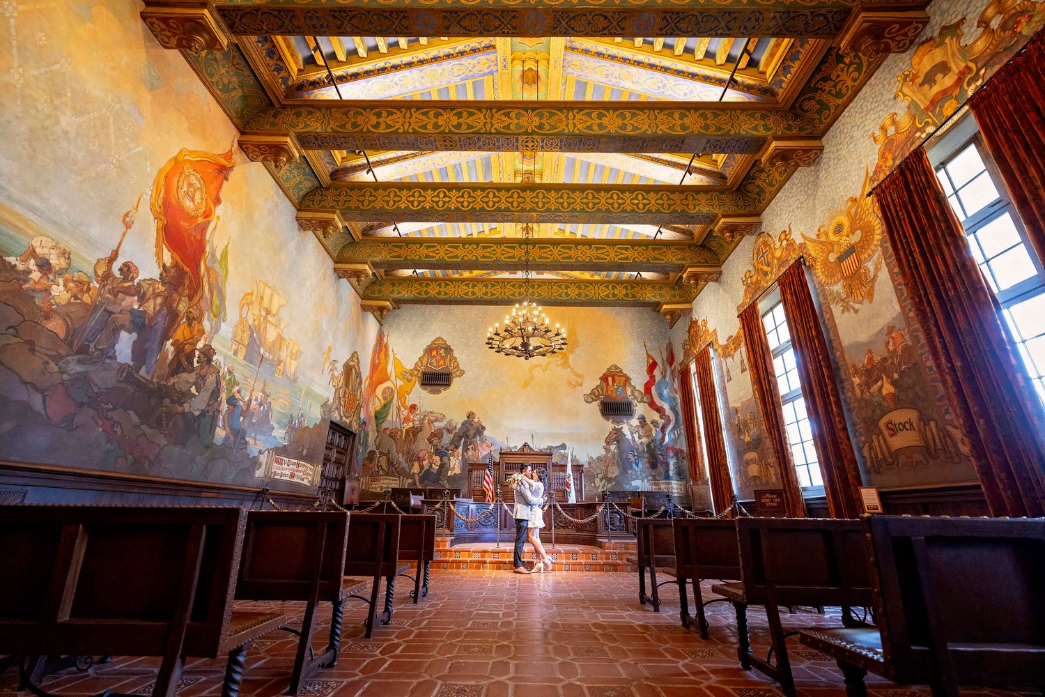 Bride and groom embrace at the front of the mural room at the Santa Barbara Courthouse