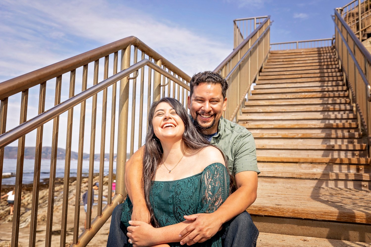 Couple laughing together while sitting on wood steps at the beach