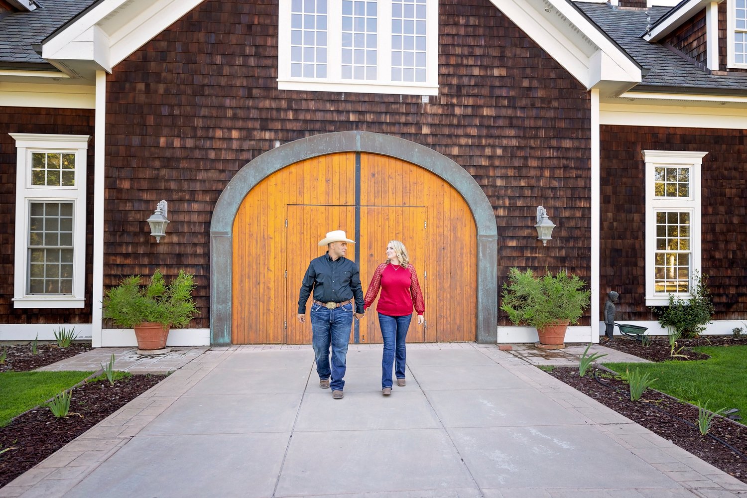 couple walking toward the camera holding hands in front of the barn doors at Spanish Oaks Ranch