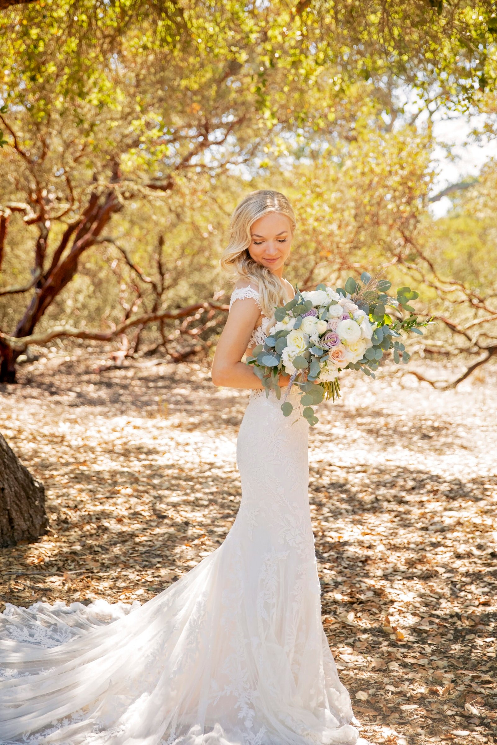 bride holding her bouquet while looking down at the back of her dress in a forest of oak and manzanita trees