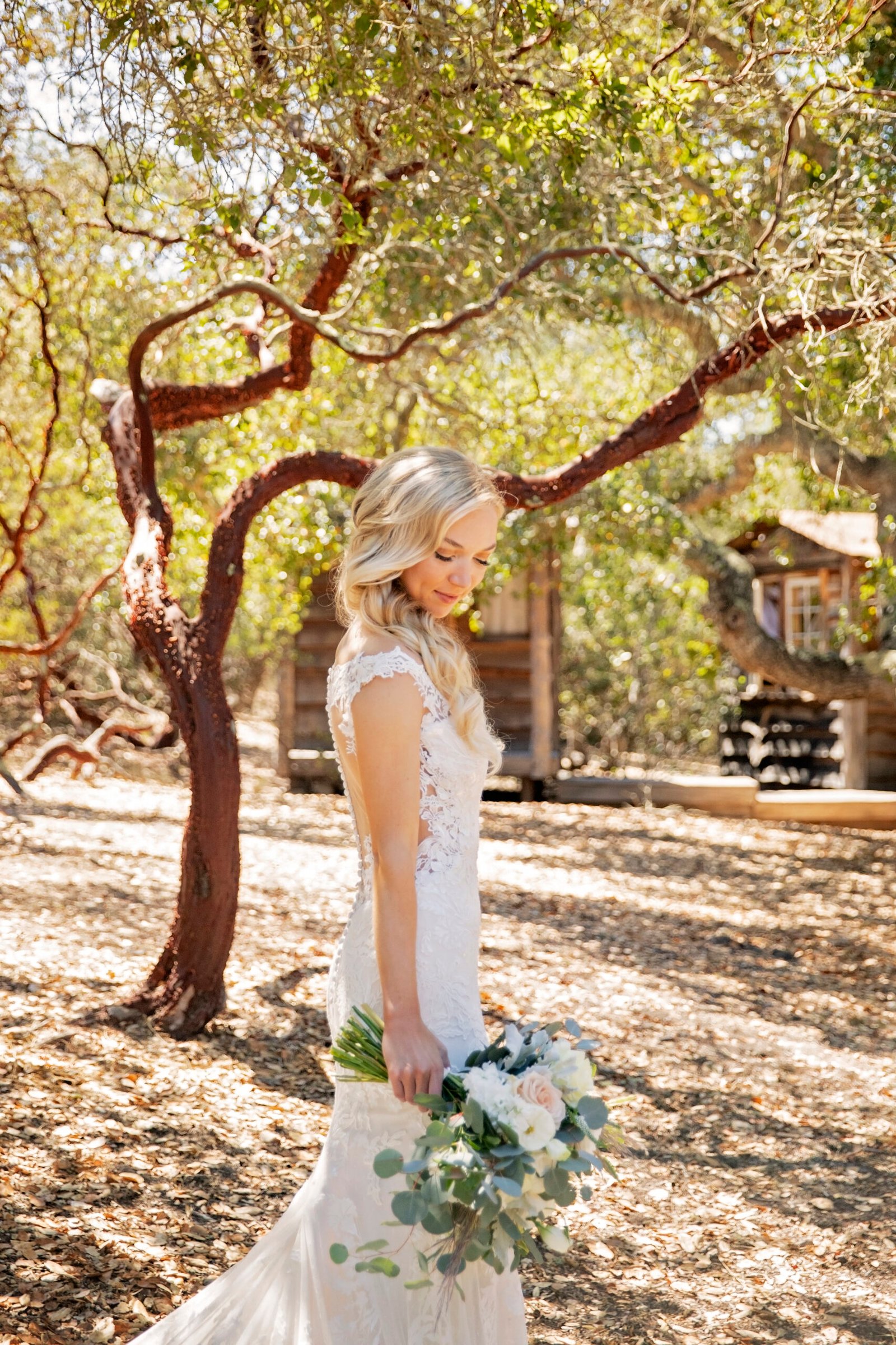 bride holding her bouquet while looking down at the back of her dress in a forest of oak and manzanita trees