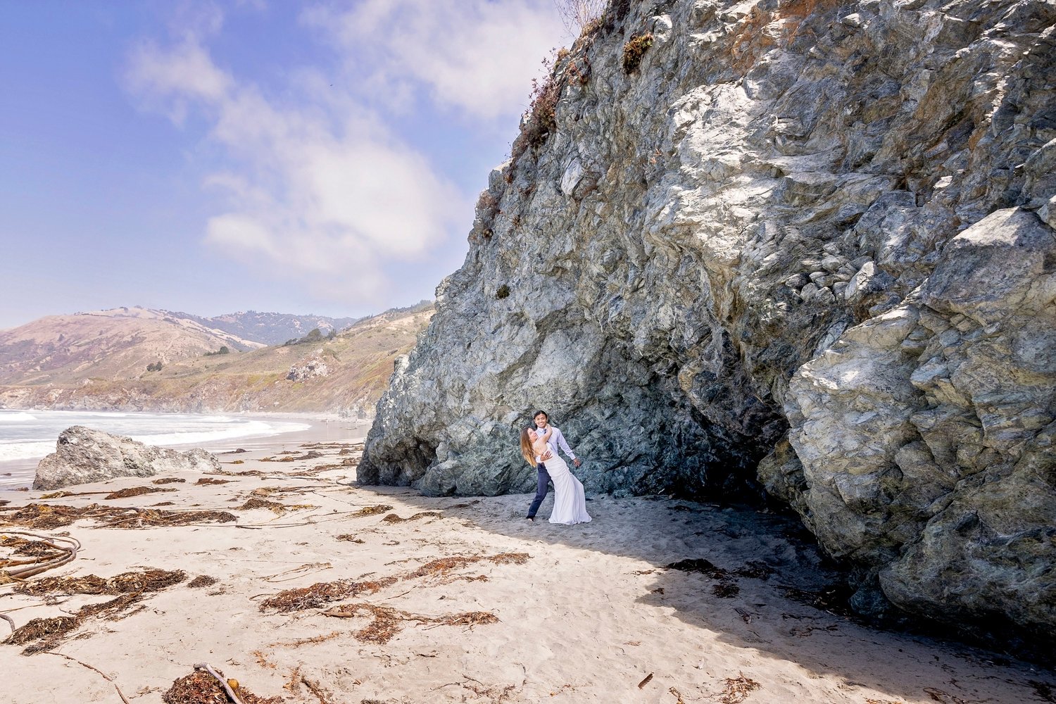 couple kissing in front of a cave rock on the beach