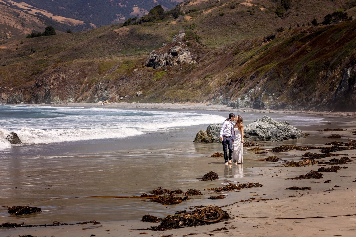 couple stopping for a kiss while walking along the beach during an engagement session