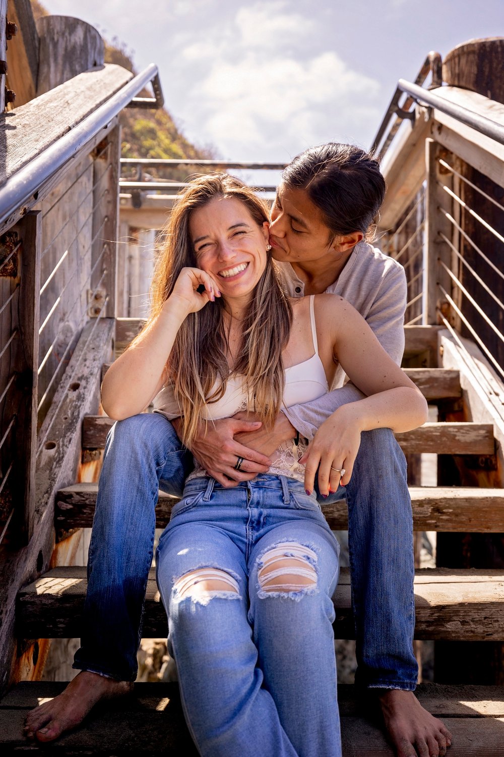 couple smiling together while sitting on the stairs in Big Sur