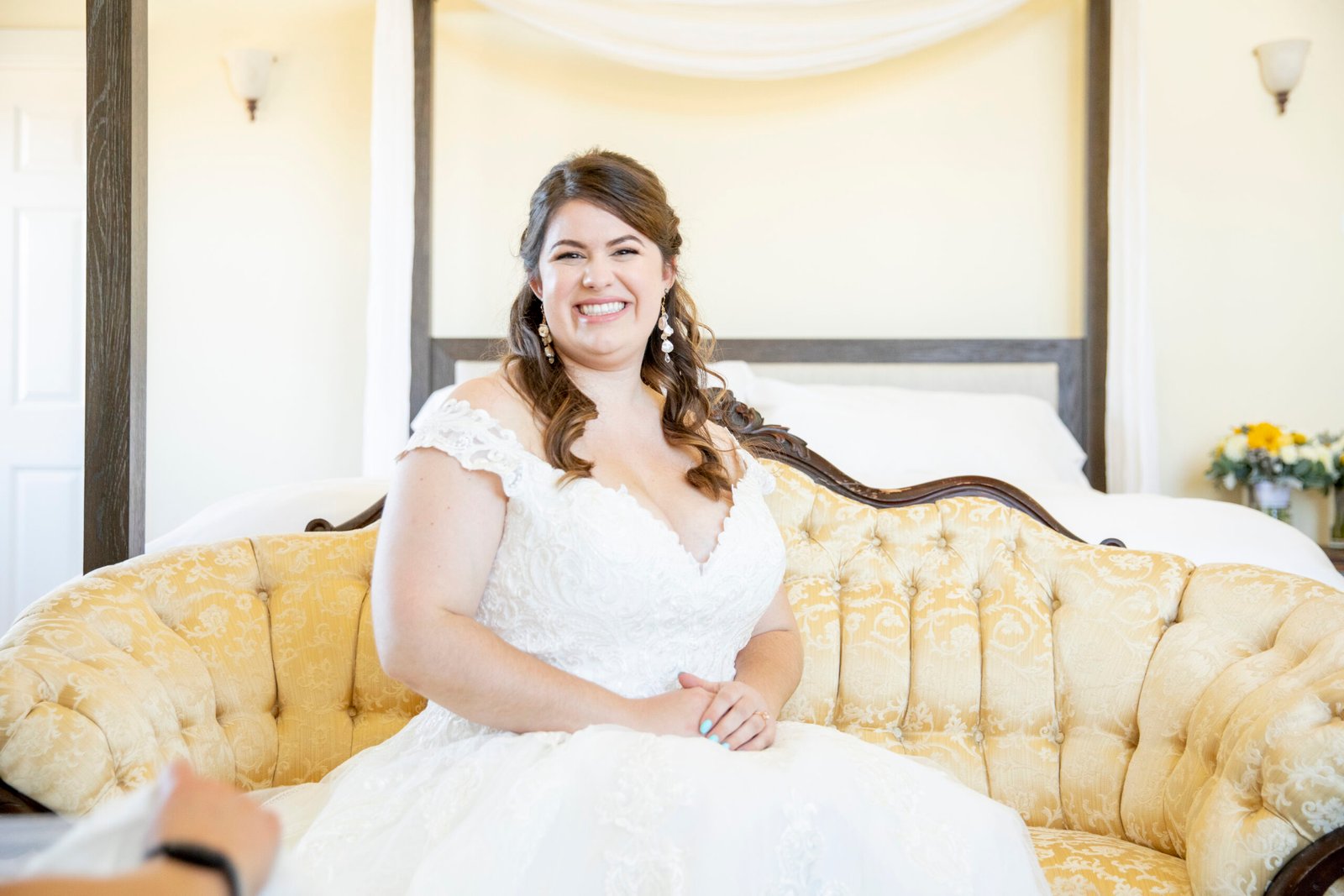 bride smiling at eh camera while sitting on an antique sofa in her wedding dress