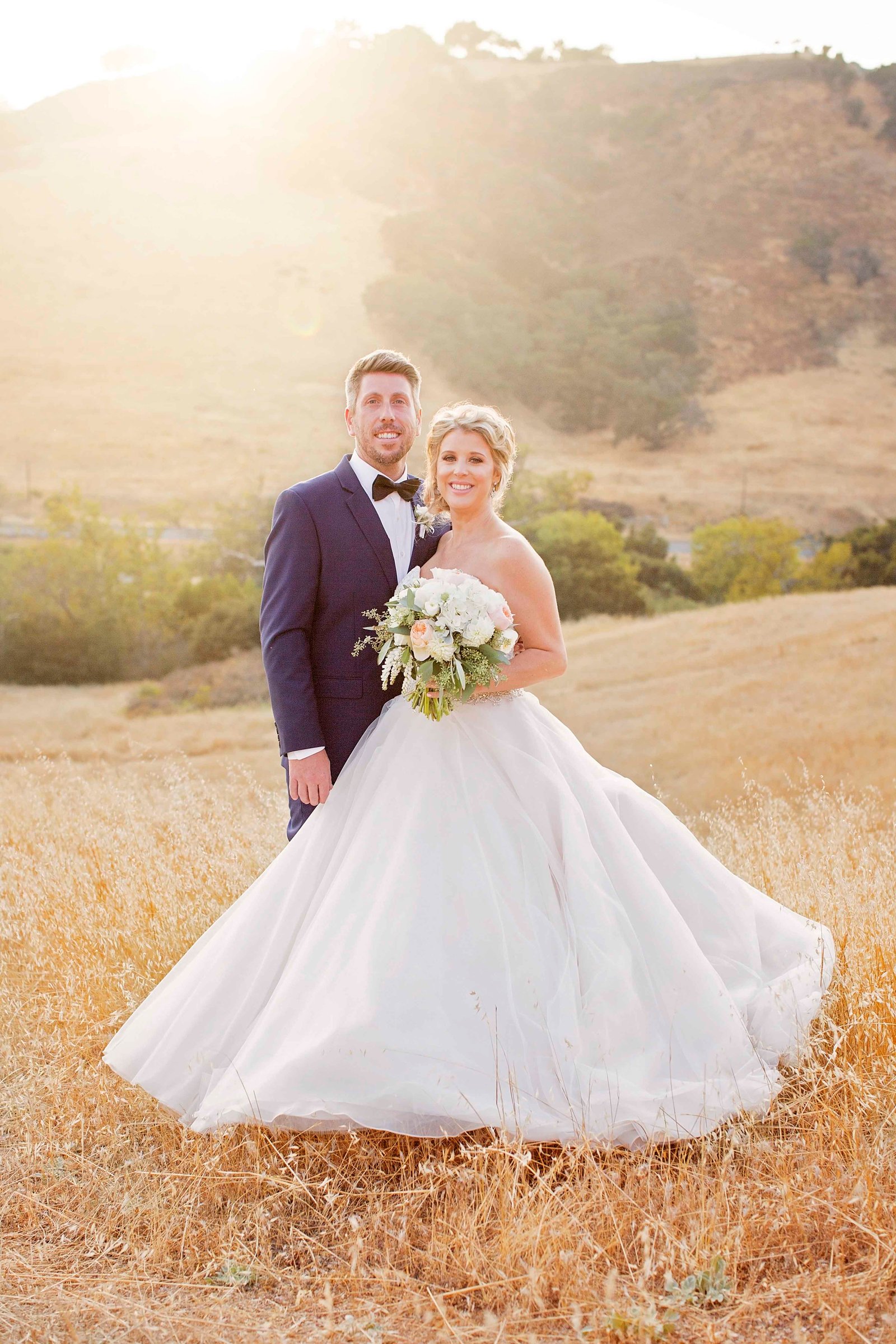 bride and groom standing in an open field at sunset at Higuera Ranch