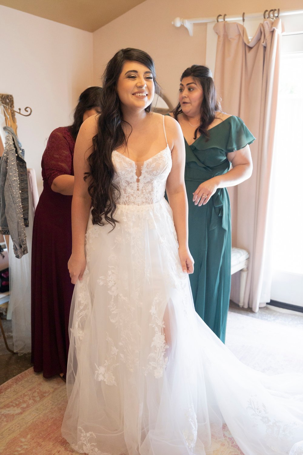 bride smiling as her mom fastens her wedding dress