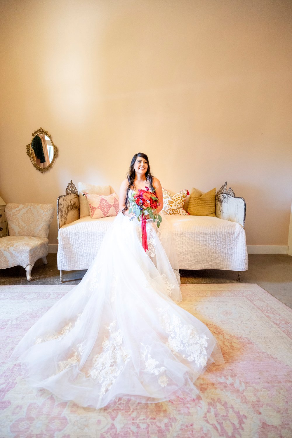 Bride smiling while holding her bouquet and sitting on a day bed