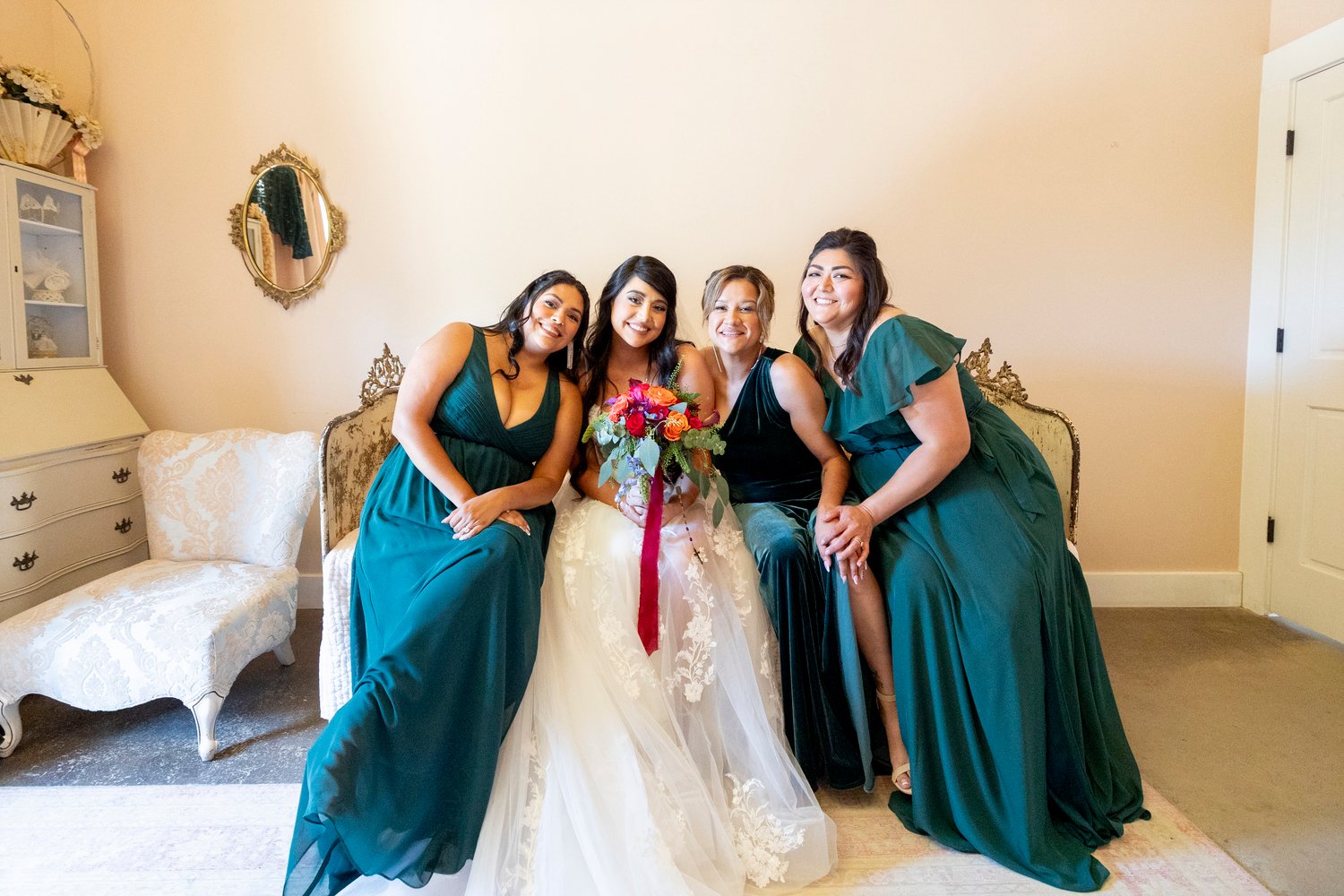 bride and bridesmaids lean in while sitting on a bed