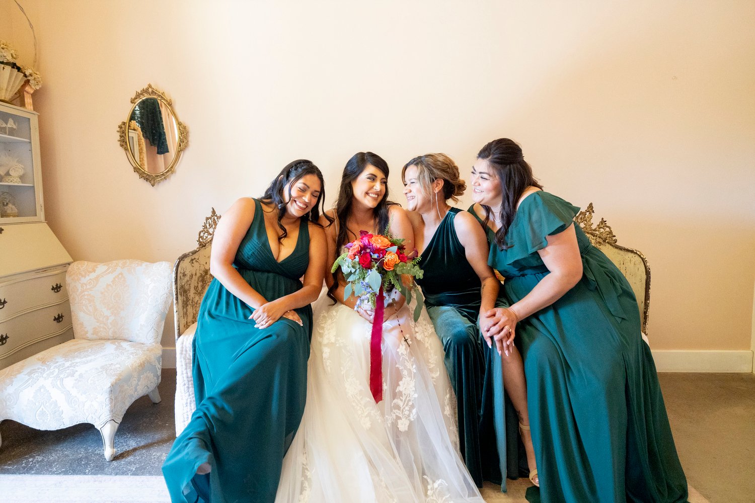 Bride smiling at a a bridesmaid while sitting on a bed
