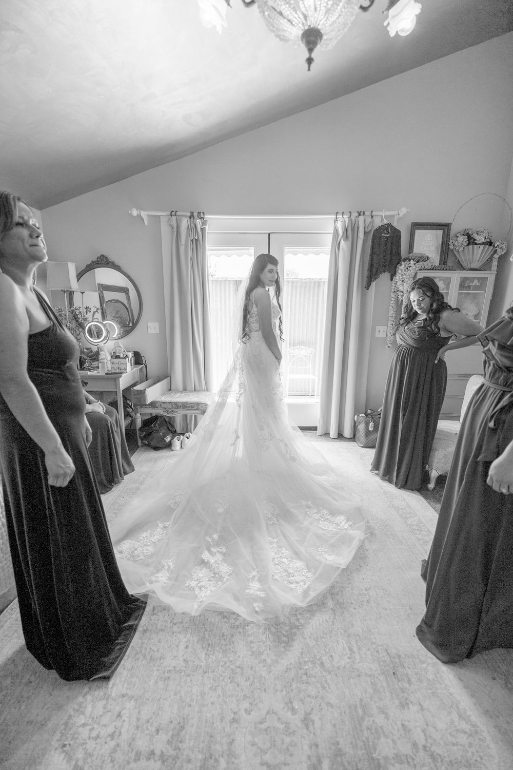 bride smiling at her bridesmaids while standing in front of a window with her dress fanned out behind her