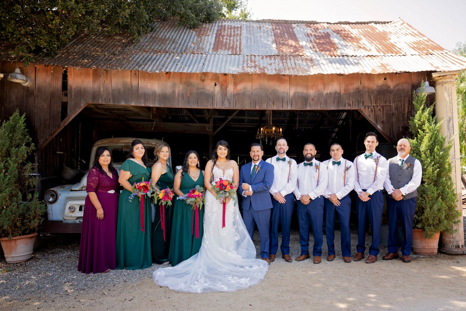 bride and groom pose with the wedding party in front of an open barn