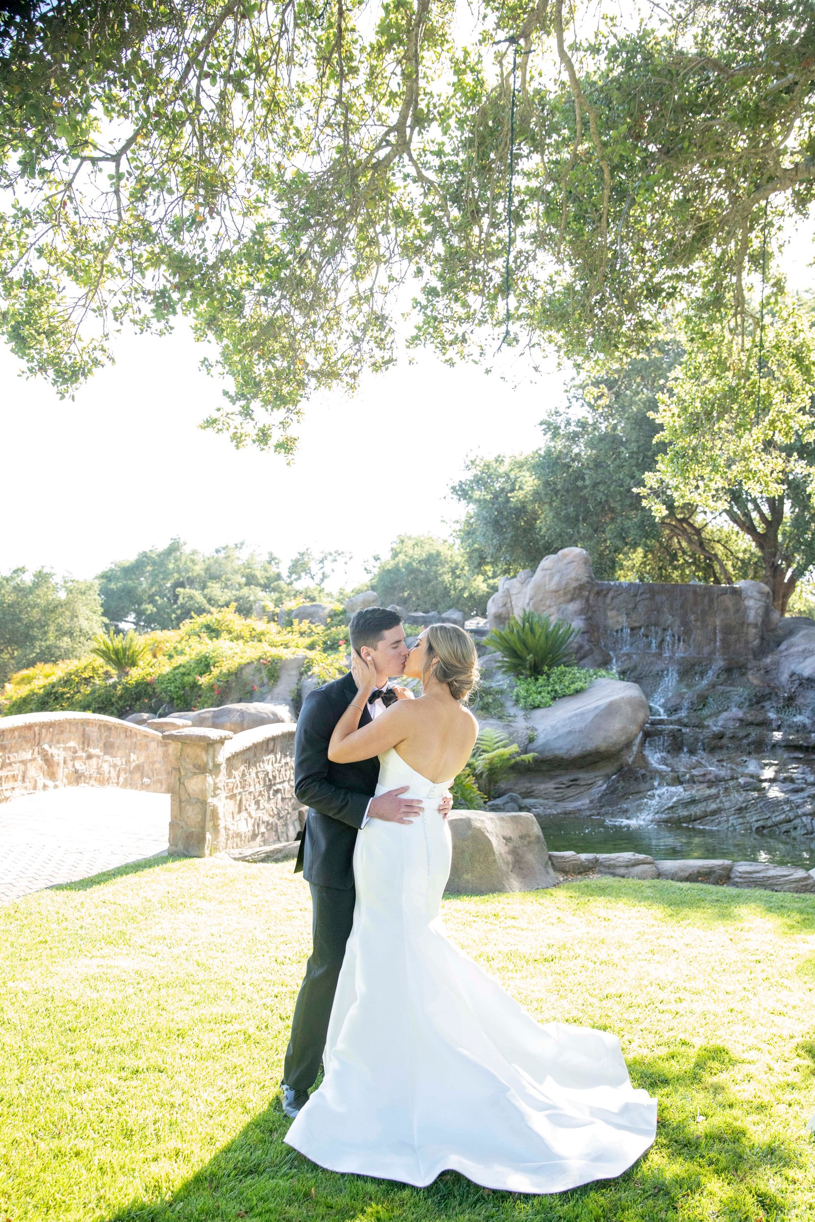 bride and groom kissing on the grass in front of a waterfall