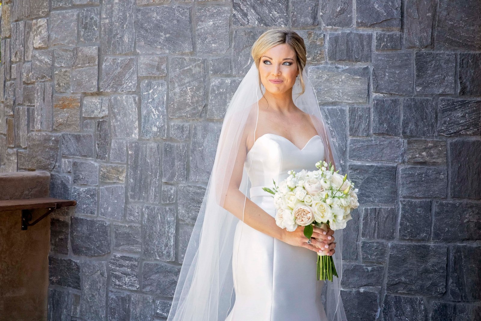 bride holding her bouquet standing in front of a stone wall