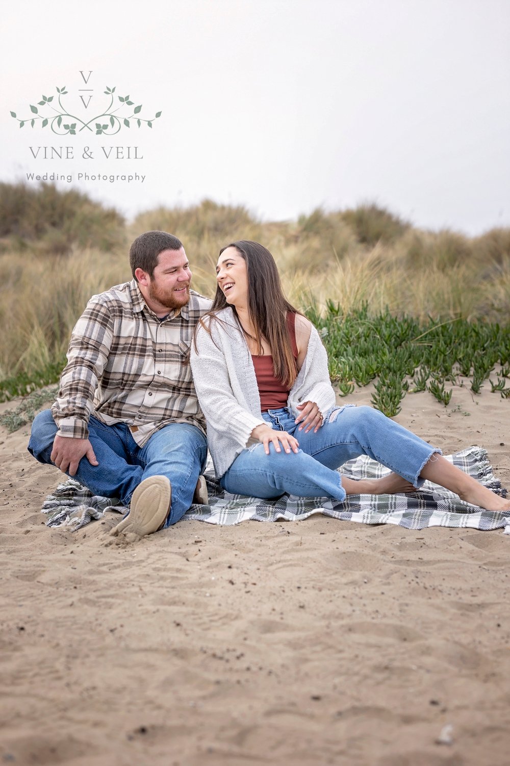 couple laughing while sitting on a blanket in the sand