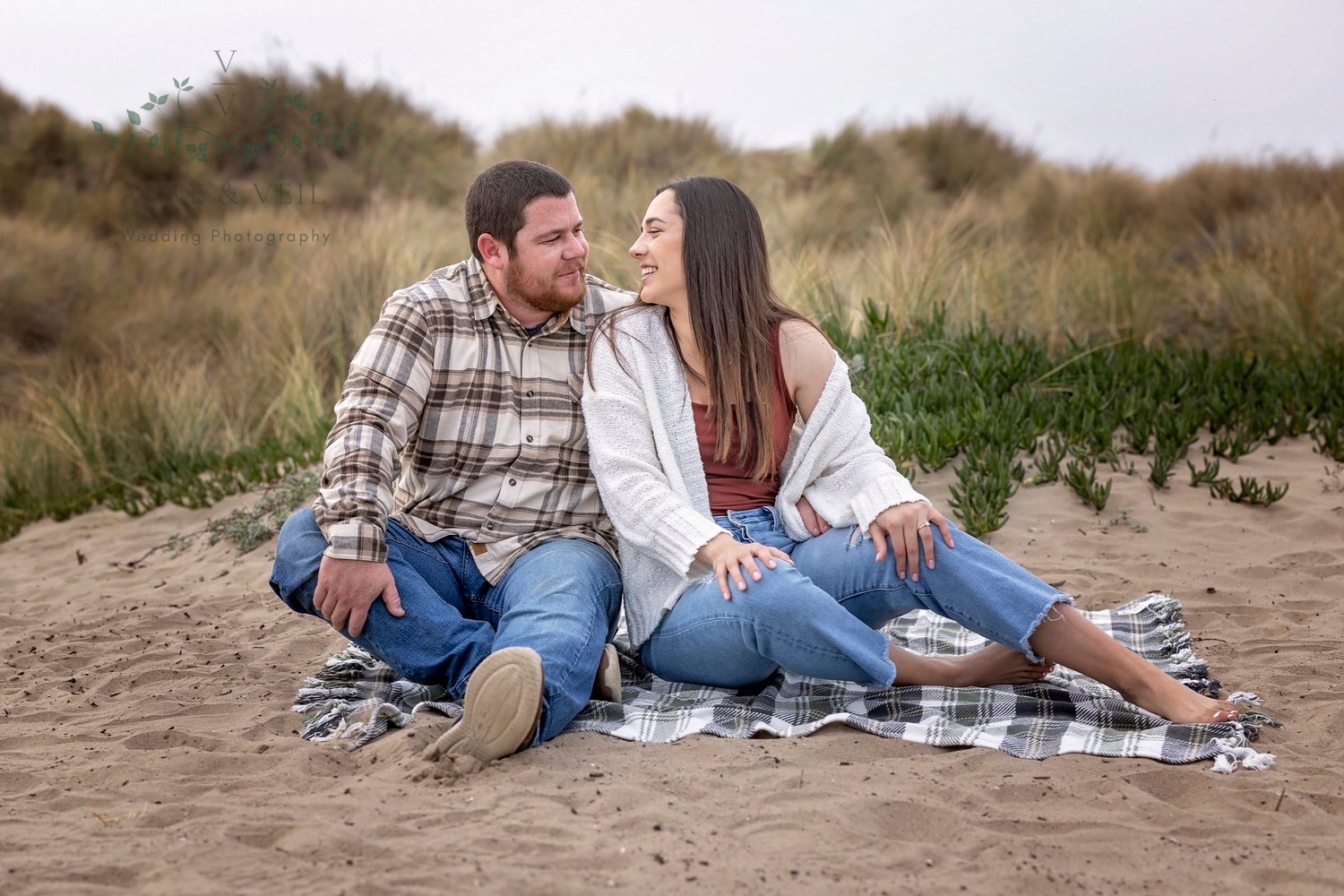 couple sitting on a blanket in the sand looking at each other