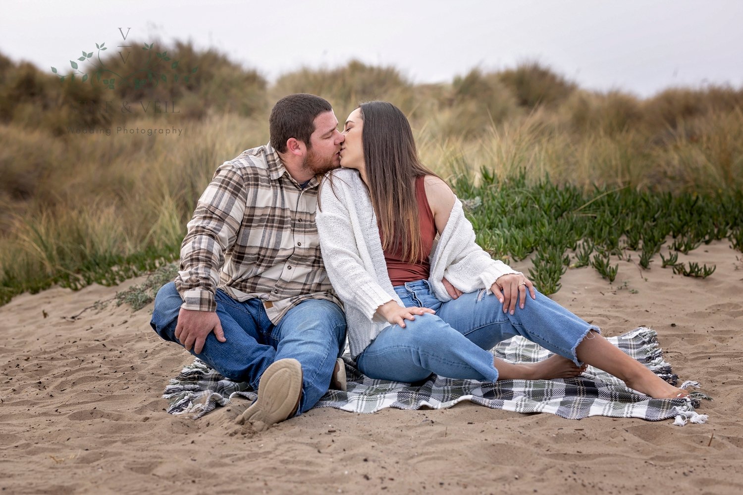 couple kissing while sitting on a blanket in the sand