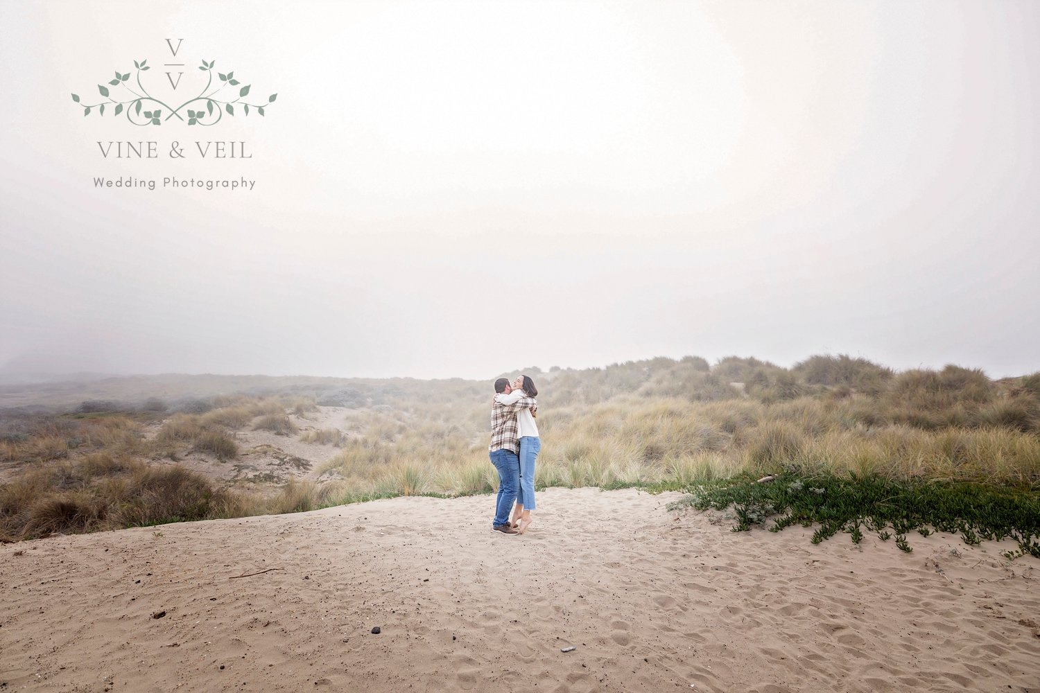 couple hugging while in the sand with beach grass