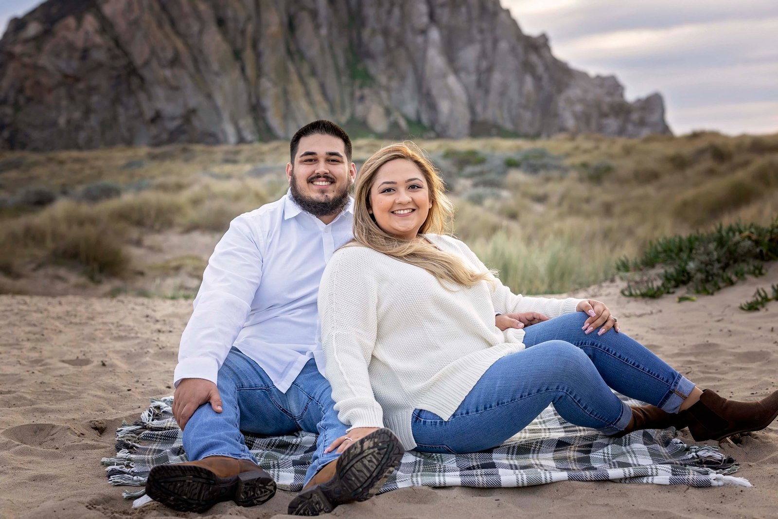 couple sitting together on a blanket in the sand during their engagement photoshoot